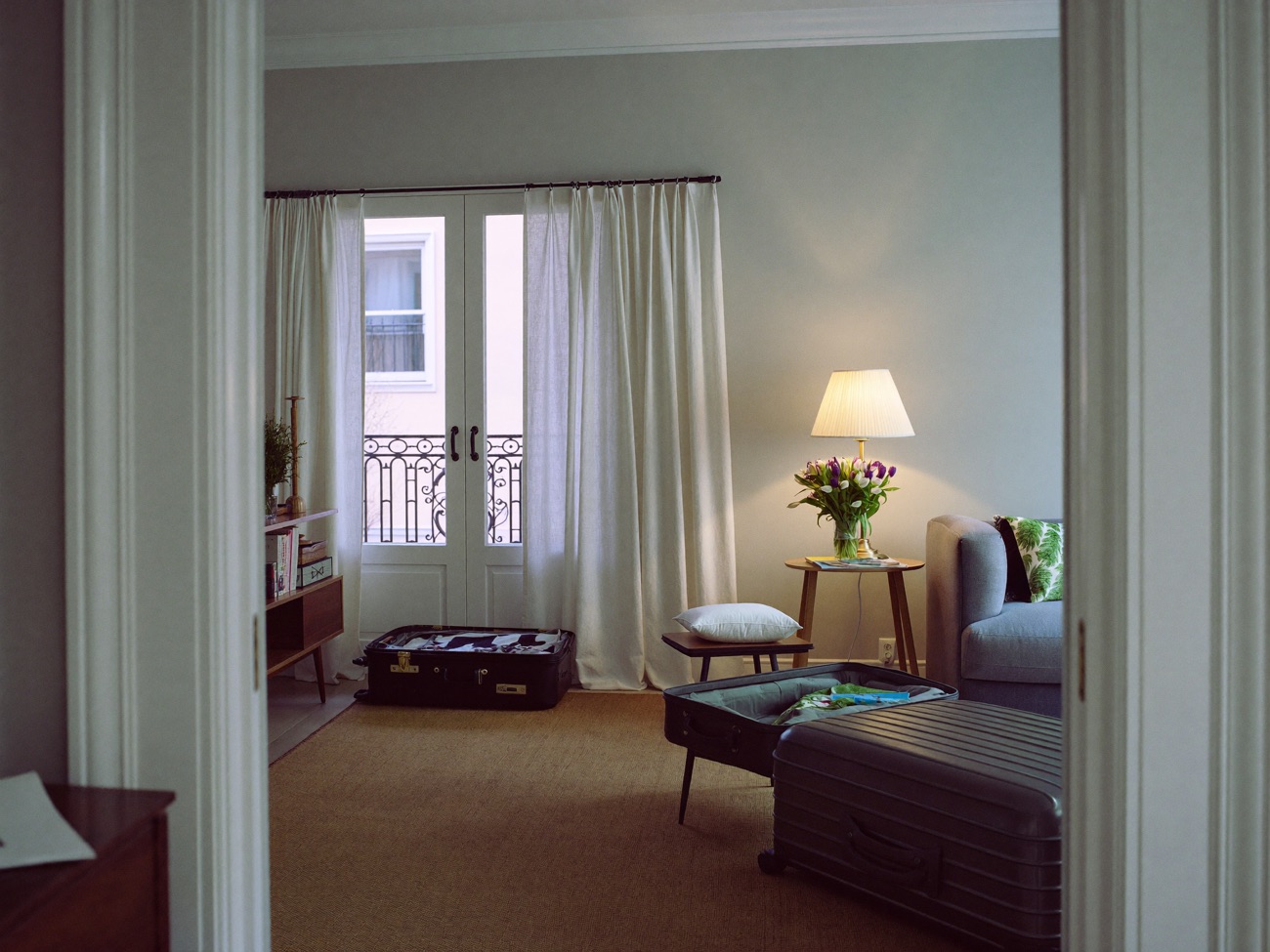 A calm living room with lamps on and a suitcase by the door